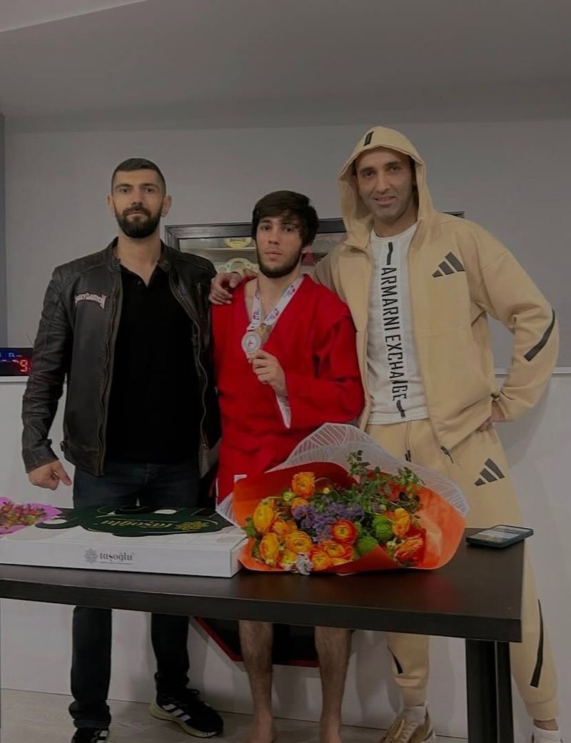 Kırmızı sambo ceketiyle madalyalı sporcu, antrenörleriyle