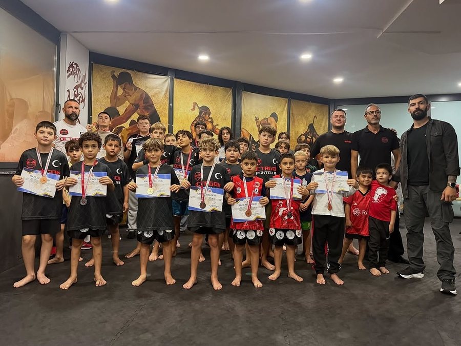 Madalya ve belgeleriyle çocuk sporcular, antrenörleriyle salonda